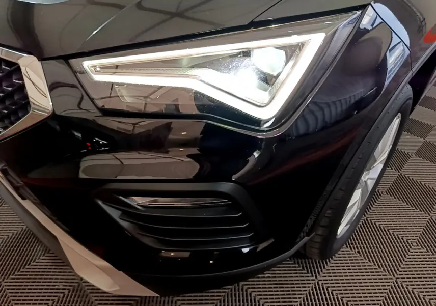 Gros plan sur le phare avant droit allumé du SEAT Ateca noir, mettant en valeur la calandre et la roue avant.