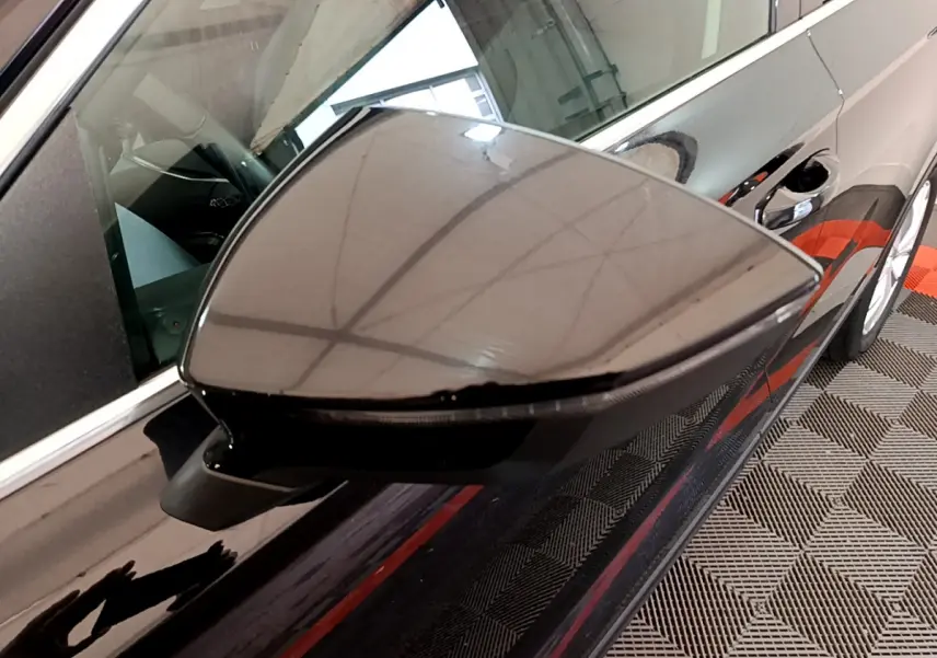 Gros plan sur le rétroviseur côté gauche noir brillant du SEAT Ateca 2022 avec reflet du plafond et carrosserie noire.