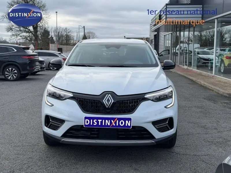 Vue frontale d'un Renault Arkana blanc 2025 avec calandre noire et logo Renault centré, sur parking extérieur.