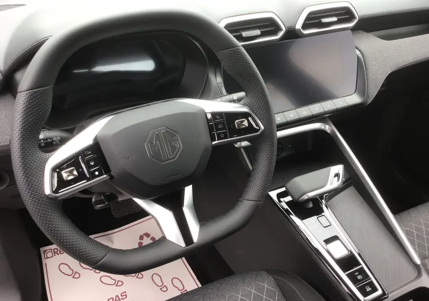 Vue intérieure centrée sur le volant noir perforé et la console centrale avec écran tactile du MG ZS 1.5 L Hybrid+ Cosmic Silver.
