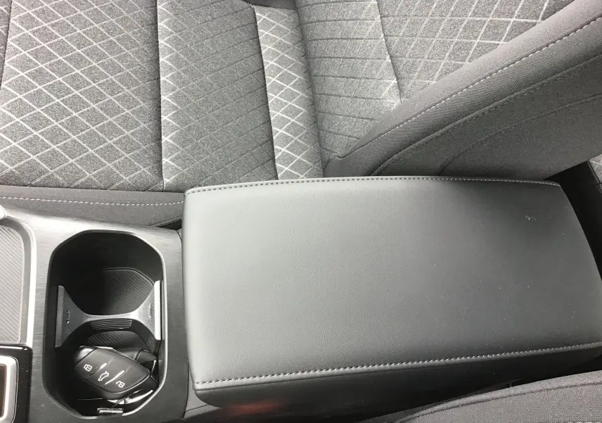 Gros plan sur l'accoudoir central noir et porte-gobelets avec clé de la MG ZS 1.5 L Hybrid+ 2026, sièges tissu gris.