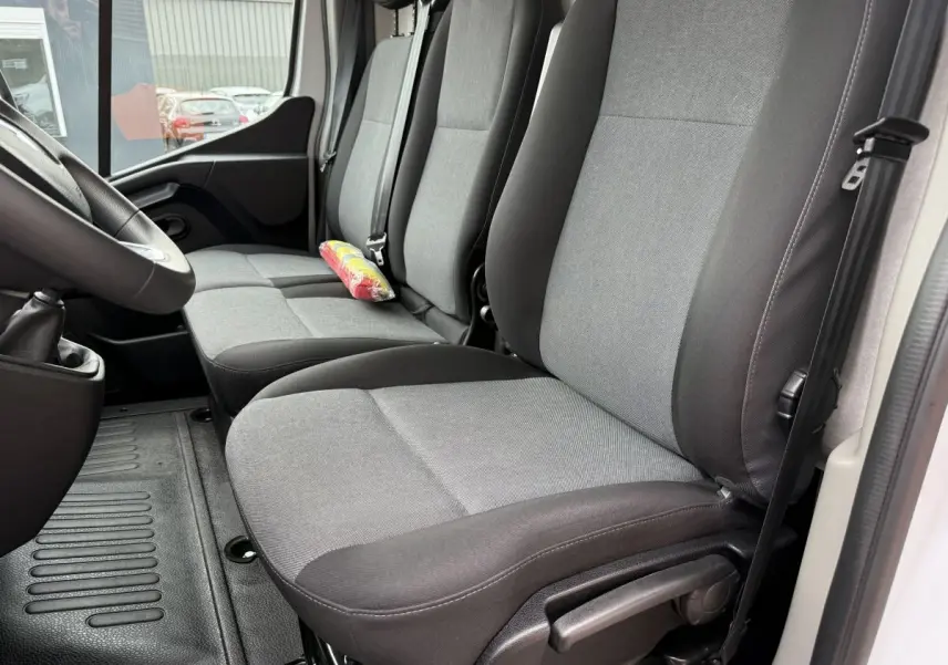 Vue intérieure côté conducteur du Renault Master blanc 2024, montrant les sièges tissu gris et noir et la ceinture de sécurité.