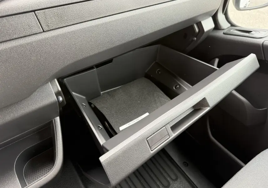 Vue rapprochée de la boîte à gants ouverte côté passager dans l’habitacle noir du Renault Master blanc 2024.