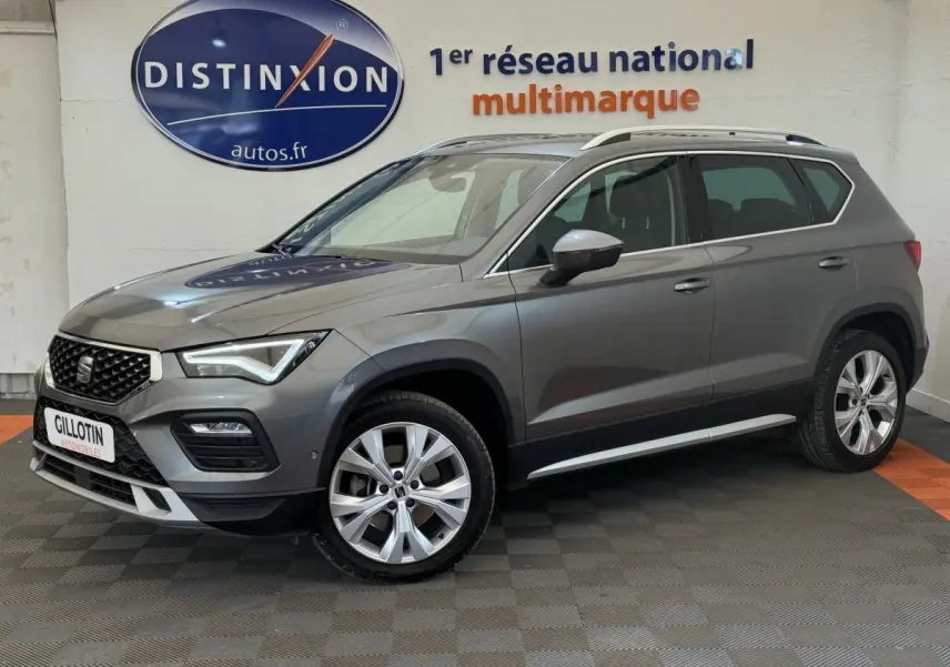Vue 3/4 avant droit d'un SUV SEAT Ateca gris clair 2023 avec jantes alliage et barres de toit chromées.