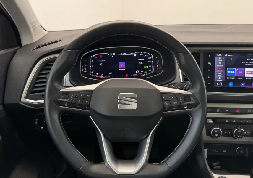Vue intérieure centrée sur le volant cuir noir du SEAT Ateca 2023 avec tableau de bord digital et écran tactile.