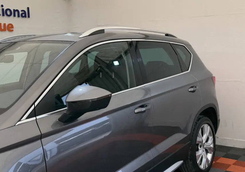 Vue côté gauche du SEAT Ateca gris clair 2023, mettant en valeur les jantes et les barres de toit chromées.