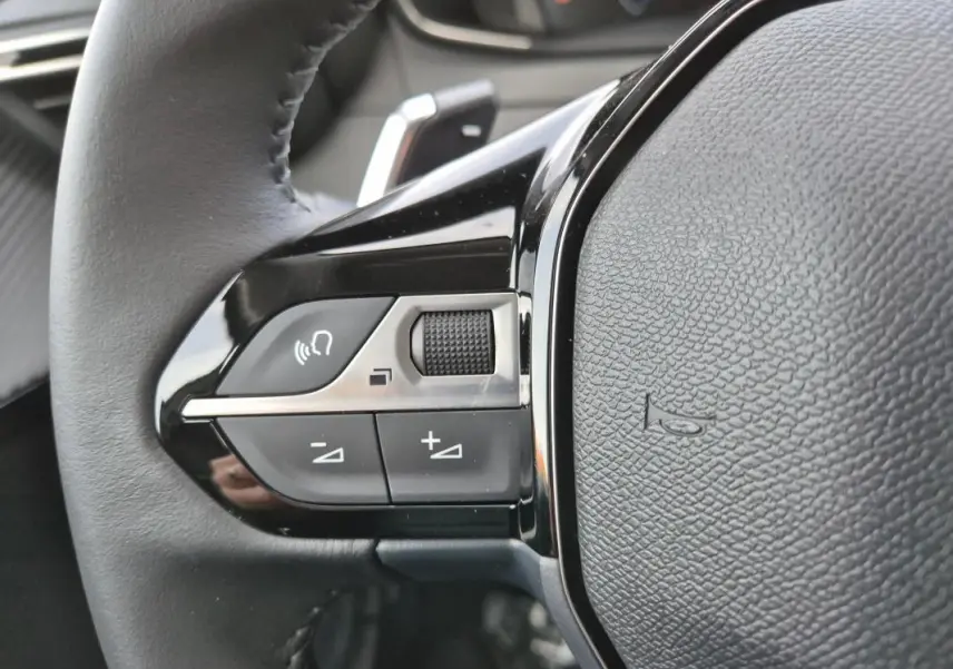 Gros plan sur les commandes gauche du volant noir de la Peugeot 208 Hybrid 110 e-DCS6 Allure blanche de 2025.