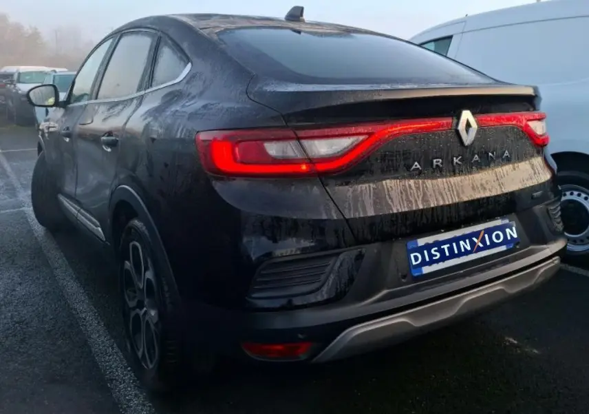 Profil côté gauche d'une Renault Arkana noire métal 2023, avec jantes bi-ton et toit incliné dans un showroom.