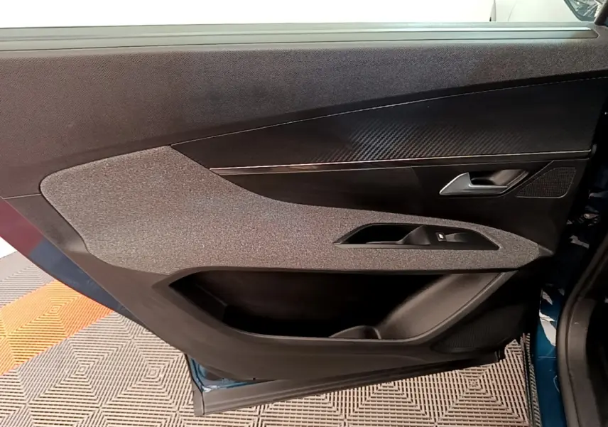 Vue rapprochée de la porte avant droite d’un Peugeot 5008 bleu, avec habillage tissu et insert imitation carbone.