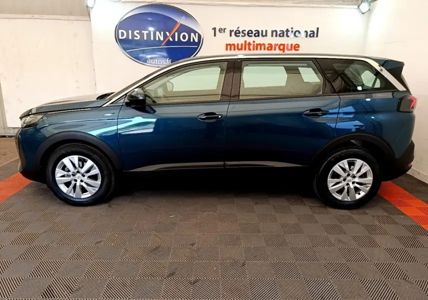 Vue de profil côté gauche d'un Peugeot 5008 bleu 2021 stationné en intérieur avec jantes alliage et vitres teintées.
