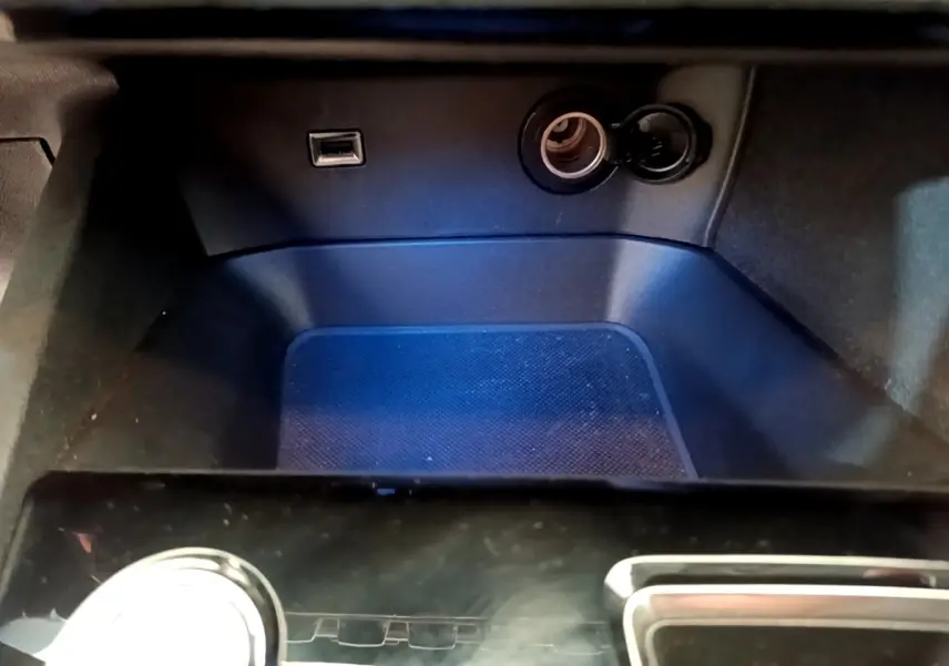 Gros plan sur la prise USB et l’allume-cigare dans le rangement avant noir du Peugeot 5008 bleu de 2021.
