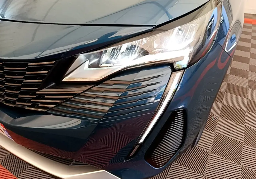Gros plan sur l'avant droit bleu du Peugeot 5008 2021, mettant en valeur le phare LED et la calandre distinctive.
