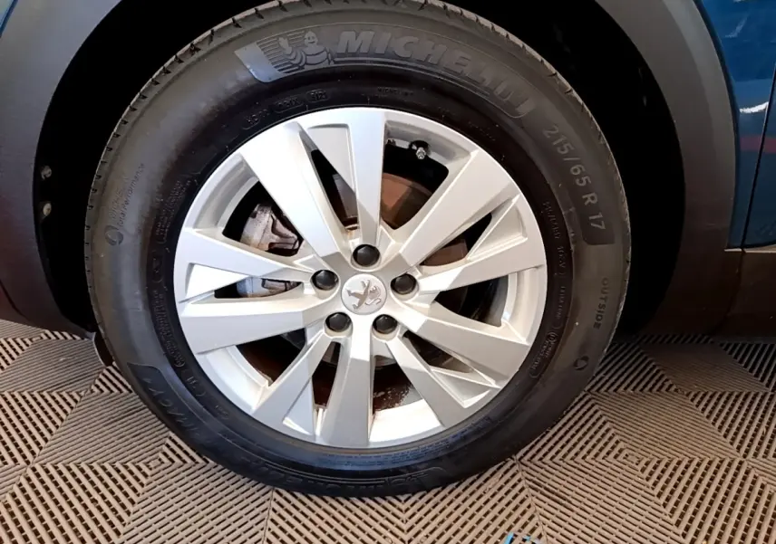 Gros plan sur la roue avant droite d’un Peugeot 5008 bleu, avec jante alliage argentée et pneu Michelin.