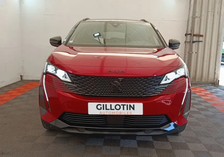 Peugeot 3008 rouge vue de face, avec calandre noire et phares LED allumés dans un garage.