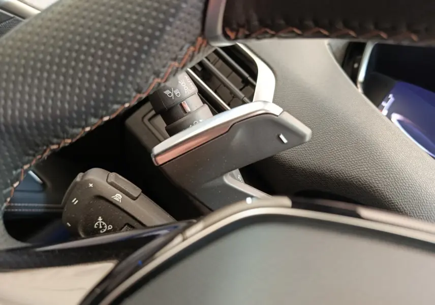 Gros plan sur palettes de changement de vitesse derrière le volant cuir noir du Peugeot 3008 rouge, version GT Pack.
