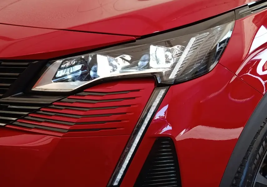 Gros plan sur l'avant droit rouge du Peugeot 3008 2022, mettant en valeur le phare LED et la calandre distinctive.
