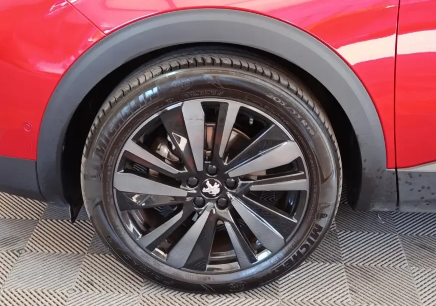 Gros plan sur la roue arrière droite d’un Peugeot 3008 rouge avec jante alliage noire brillante et logo lion central.