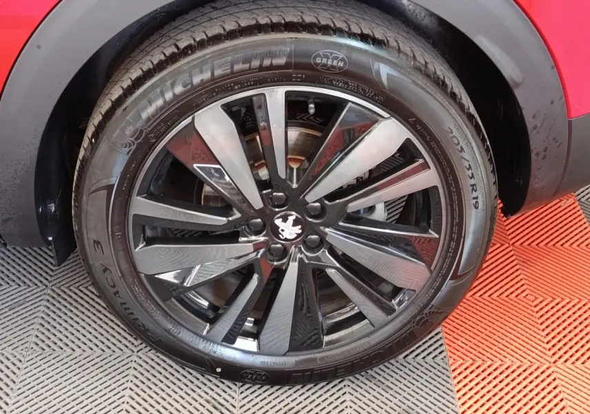 Gros plan sur la roue avant droite d’un Peugeot 3008 rouge avec jante alliage noire et logo lion au centre.