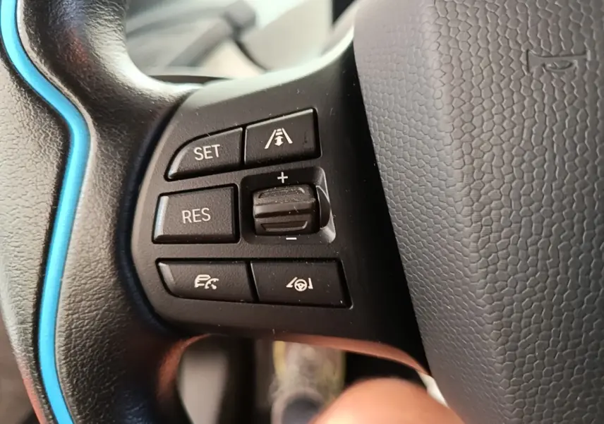 Gros plan sur les commandes de régulateur de vitesse au volant cuir noir avec surpiqûre bleue d'une BMW i3 120 Ah Atelier.
