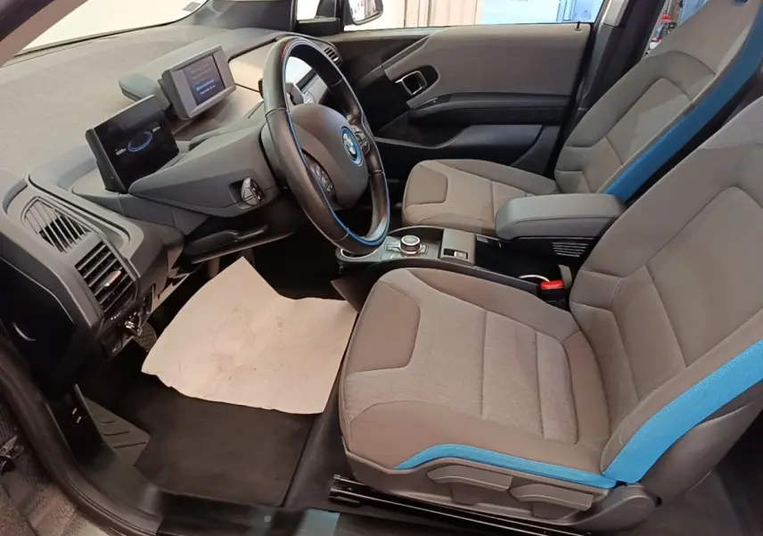 Vue intérieure côté conducteur de la BMW i3 120 Ah avec sièges gris et bleu et tableau de bord moderne.