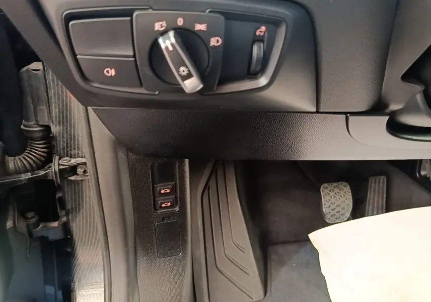 Vue intérieure côté gauche du poste de conduite d'une BMW i3 noire, avec commandes d'éclairage et pédales visibles.