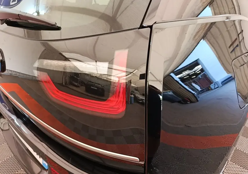 Gros plan sur le feu arrière gauche rouge d’une BMW i3 noire, reflétant l’intérieur d’un garage.