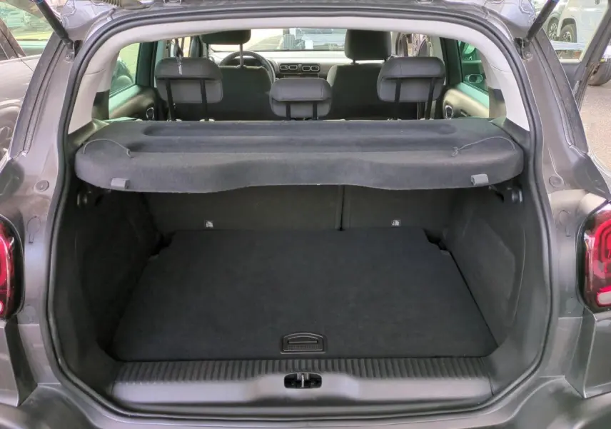 Vue arrière du coffre ouvert d'un Citroën C3 Aircross gris foncé avec cache-bagages et sièges arrière visibles.