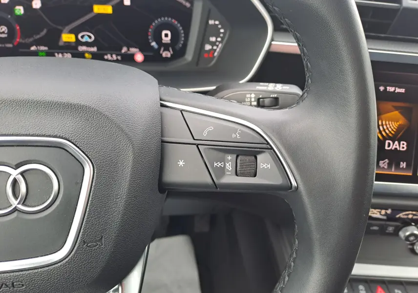 Gros plan sur le volant cuir noir de l’Audi Q3 35 TDI 2023 avec commandes audio intégrées et tableau de bord numérique.