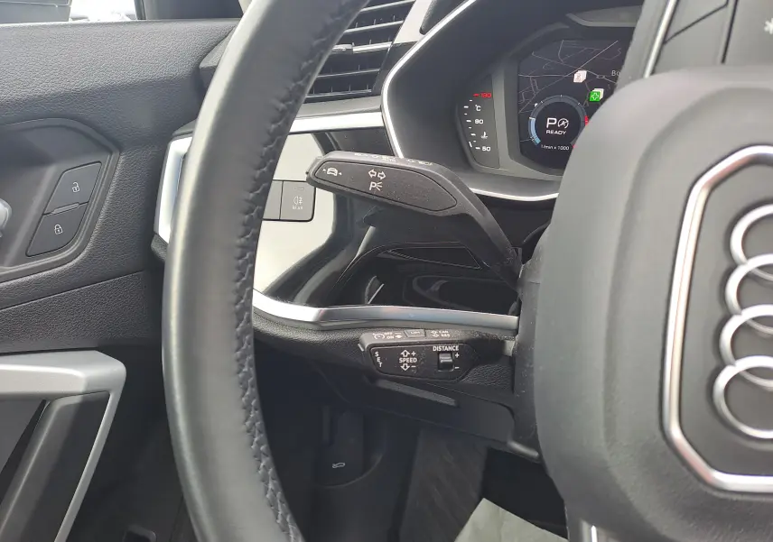 Vue rapprochée du volant côté gauche de l'Audi Q3 gris nano, avec commandes au volant et tableau de bord numérique.