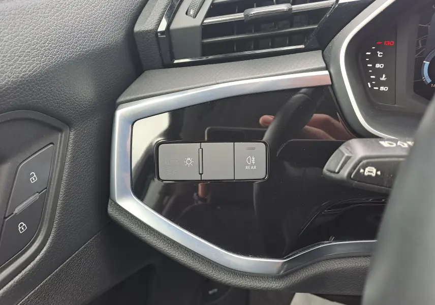 Gros plan sur les commandes d'éclairage à gauche du volant dans l'habitacle noir de l'Audi Q3 35 TDI 2023.