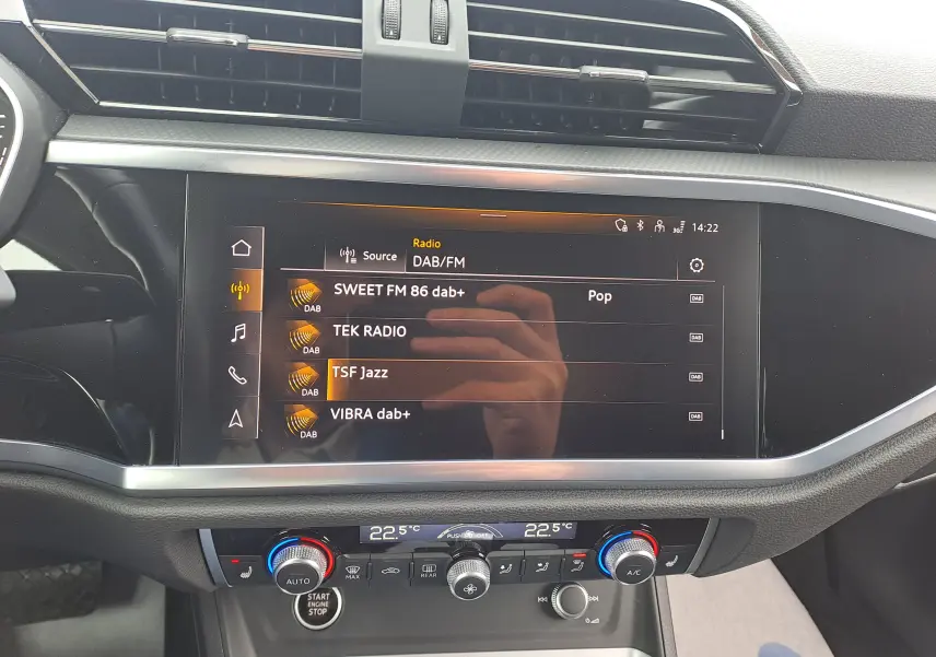 Vue intérieure centrée sur l’écran tactile multimédia et la console de climatisation d’un Audi Q3 gris Nano 2023.
