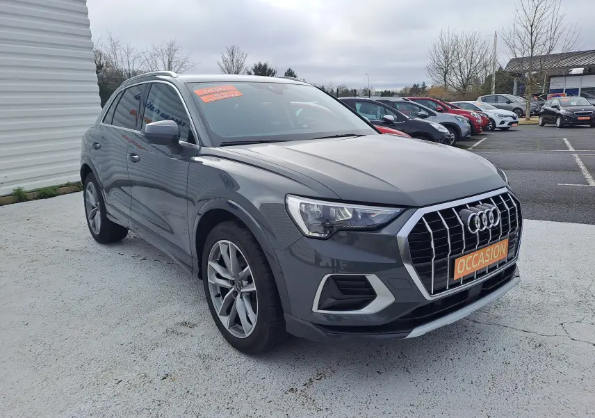 Audi Q3 gris nano en 3/4 avant droit, avec calandre chromée et jantes alu 19 pouces visibles, sur parking extérieur.