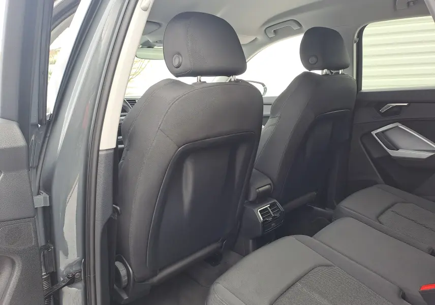 Vue intérieure arrière côté gauche de l'Audi Q3 35 TDI gris nano, sièges tissu noir et aérateurs centraux visibles.
