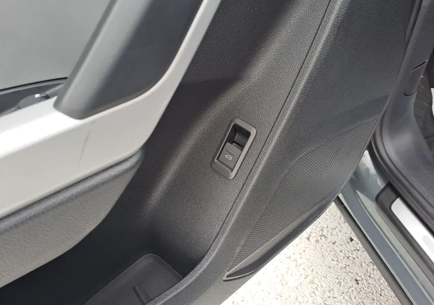 Détail de la porte avant gauche de l'Audi Q3 gris nano, montrant le bouton d'ouverture du coffre et le haut-parleur intégré.