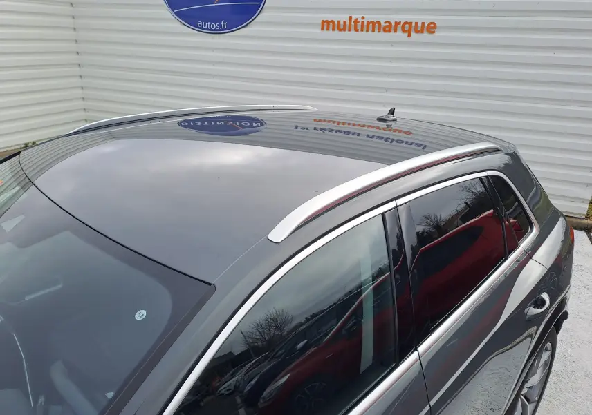 Vue plongeante sur l'arrière droit d'un Audi Q3 gris nano avec barres de toit argentées et vitres teintées.