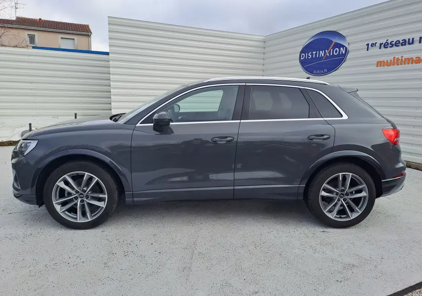 Profil droit d’un Audi Q3 35 TDI gris nano avec jantes alu 19 pouces, stationné devant un mur blanc.
