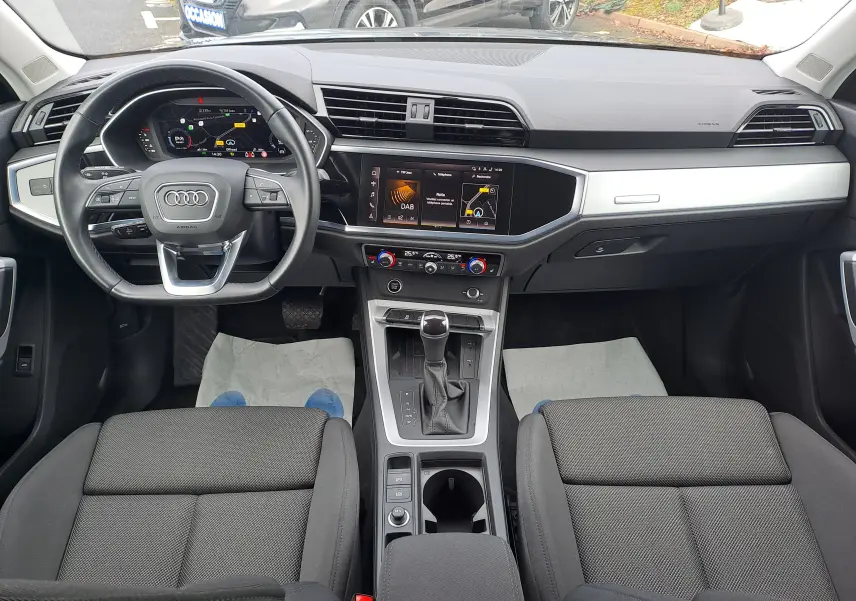 Vue intérieure frontale de l’Audi Q3 35 TDI 2023, tableau de bord moderne avec écran digital et sièges tissu noirs.