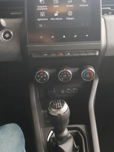 Vue centrale de l'intérieur de la Renault Clio 2025 gris, avec écran tactile, commandes climatisation et levier de vitesse manuel.