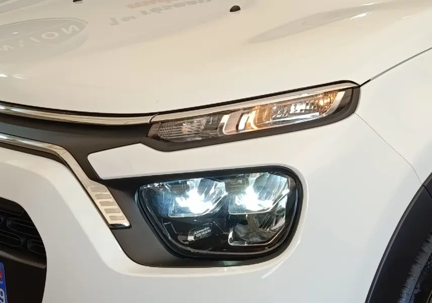 Gros plan sur l'avant droit blanc d'une Citroën C3 2022 avec phares LED allumés et calandre noire.