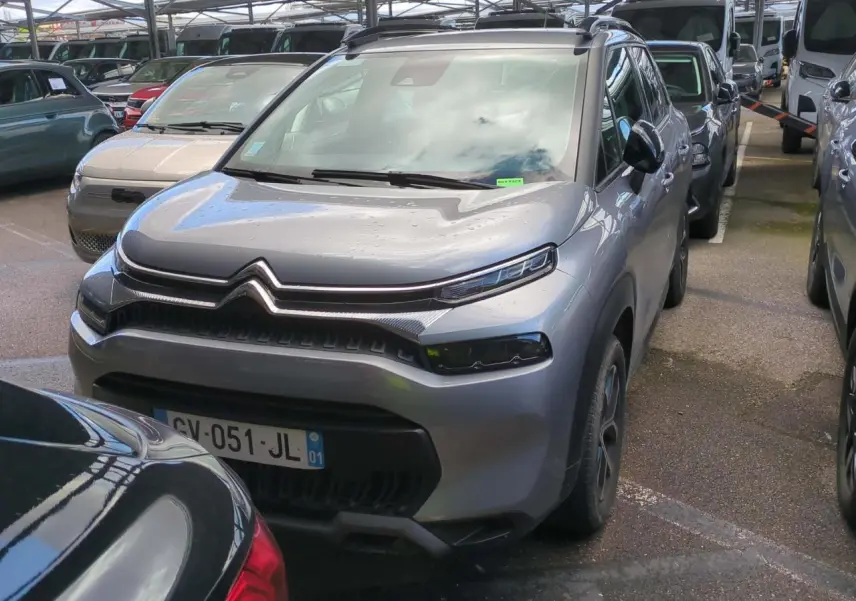 Citroën C3 Aircross gris foncé vue 3/4 avant droit avec barres de toit noir brillant en parking couvert.