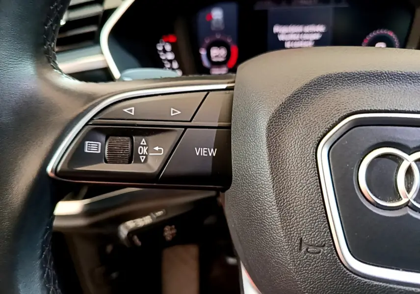 Gros plan sur le volant cuir noir d'un Audi Q3 2021 avec commandes multifonctions et logo Audi visible au centre.