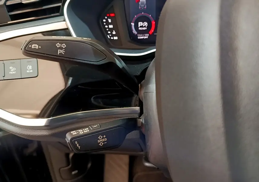 Gros plan sur les commandes au volant d'un Audi Q3 noir 2021, affichage digital et leviers multifonctions visibles.