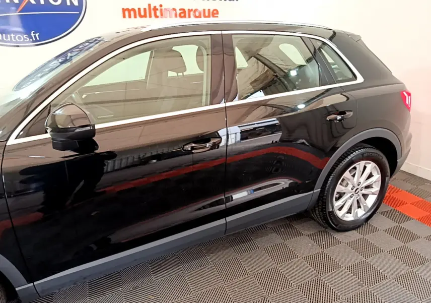 Profil côté gauche noir brillant de l'Audi Q3 35 TDI 150 S Tronic Business Line avec jantes argentées en intérieur showroom.