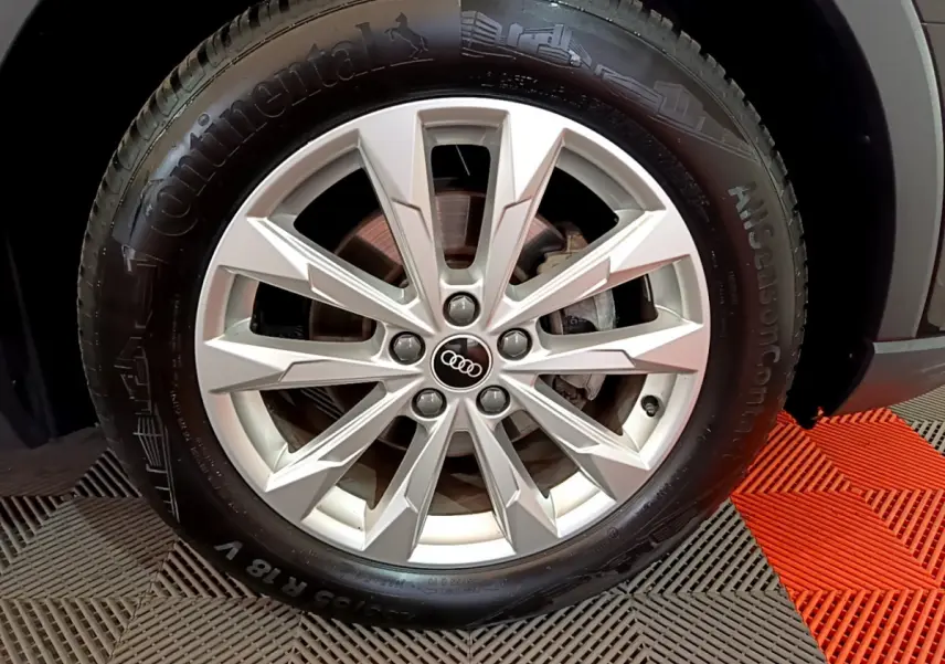 Gros plan sur la roue avant droite d'un Audi Q3 noir, mettant en valeur la jante argentée à design moderne.