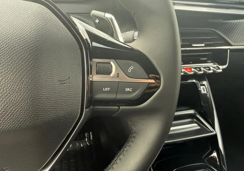 Gros plan sur le volant noir et les commandes multimédia du Peugeot 208 Hybrid 145 Allure, intérieur moderne et épuré.