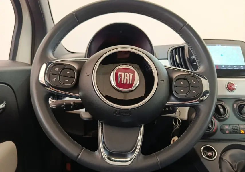 Vue rapprochée du volant cuir noir multifonctions d'une Fiat 500 blanche avec tableau de bord et écran tactile visible.