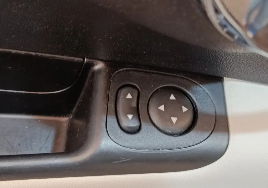 Gros plan sur les commandes de réglage des rétroviseurs intérieures noires sur panneau beige d'une Fiat 500 blanche.