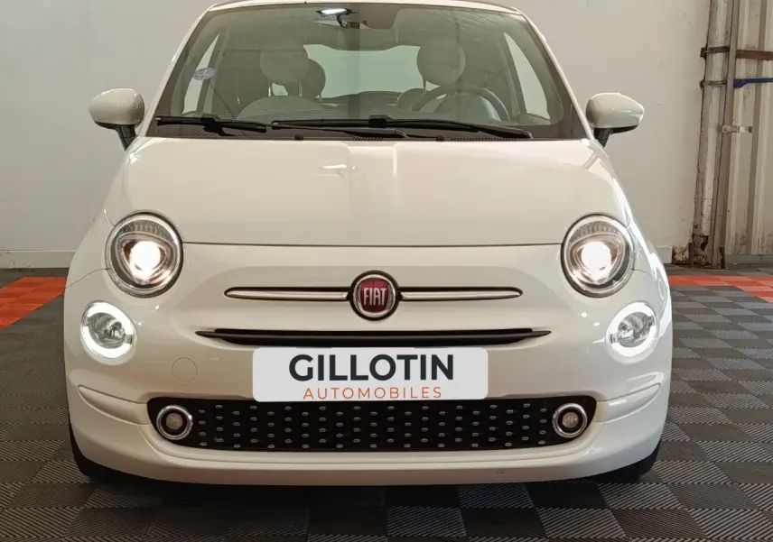Vue frontale d'une FIAT 500 blanche avec phares allumés et calandre noire à motifs ovales.