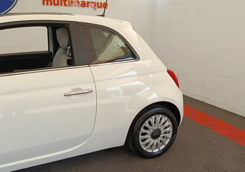 Profil arrière droit de la FIAT 500 blanche, mettant en valeur la roue et la porte arrière dans un intérieur showroom.