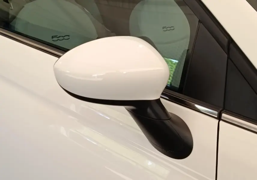 Rétroviseur côté gauche blanc de la Fiat 500 Hybrid 2022 avec sièges clairs et logo 500 visible à l'intérieur.